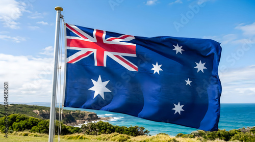 Australian flag waving strongly near coastal landscape with clear blue sky
