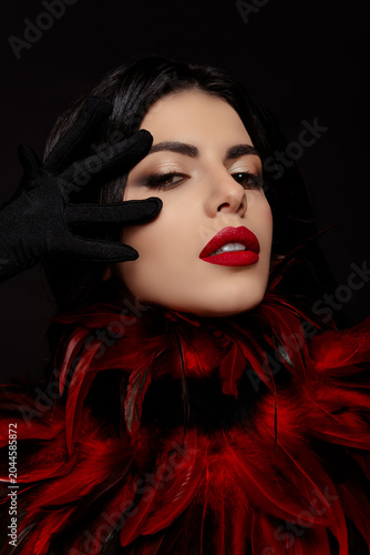 Passionate brunette woman in luxurious costume with vibrant red feathers showcasing beauty and mystery