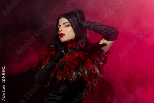Glamorous Woman in Vibrant Feathered Ensemble Posing Elegantly in a Mysterious Smoky Atmosphere