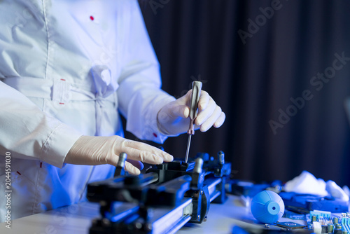 A technician adjusts and repairs equipment on a table using tools in a lab at night