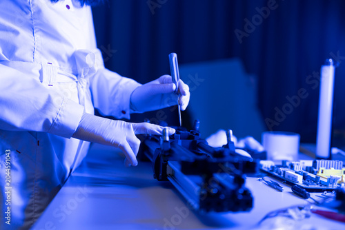 A person with gloves is assembling a device in a workshop. Tools and materials are scattered on the table