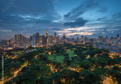 Vibrant Cityscape at Dusk Overlooking Lush Green Park with Illuminated Buildings and Dramatic Clouds during Twilight Hour Capturing Urban Serenity and Modern Architecture