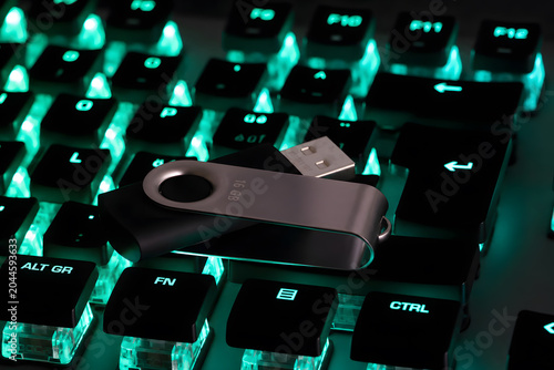 Gros plan d’une clé USB métallique de 16 Go posée sur un clavier mécanique d’ordinateur rétroéclairé en turquoise. Concept de stockage de données, sauvegarde informatique, transfert de fichiers, cyber
