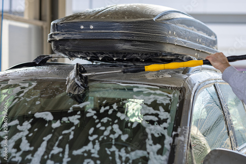 Bild auf Leinwand Man cleaning the windshield of a silver car with a long yellow brush and white soap foam at a self service wash station