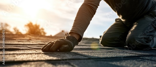 Roofer installs shingles under warm sunset glow