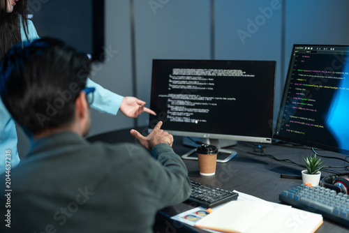 Developers Pointing At Code On Monitor In Dark Office