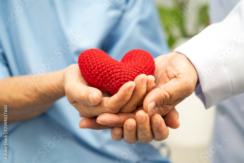 Asian woman doctor holding red heart with senior patient for health in hospital.