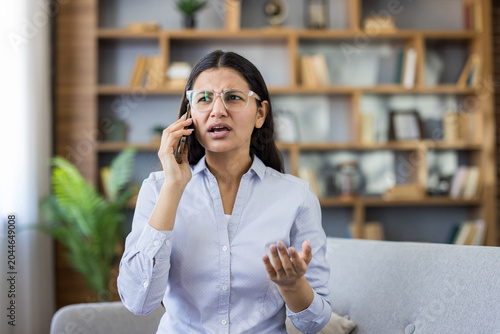 Obraz na plátně Stressed young indian woman on a couch in a home office, talking on her mobile p