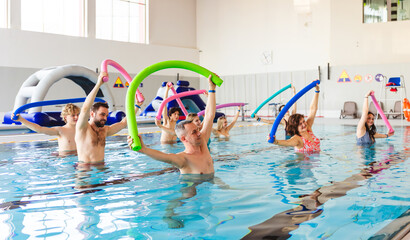 Group of people of various ages participating in an aqua aerobic class in an indoor swimming pool