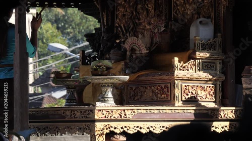 Balinese Hindu offering ceremony, with a woman placing flowers and incense on a ceremonial tray. Rising smoke creates a spiritual atmosphere during a temple ritual in Bali, Indonesia