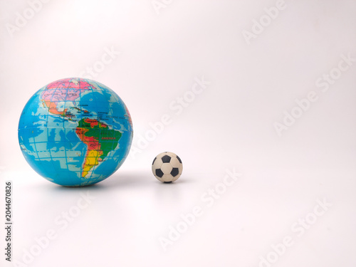A small black and white soccer ball sits on a white surface next to a colorful toy world globe