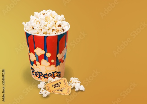 Popcorn bucket with movie tickets and spilled kernels on a yellow background with copy space