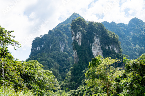 Quadro su tela Majestic limestone karst mountains covered in lush green rainforest, bathed in soft daylight under a partly cloudy sky, showcasing dramatic cliffs and dense vegetation