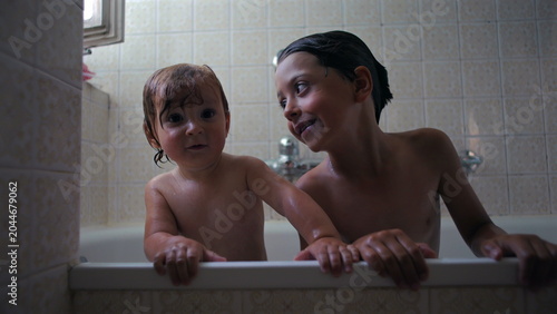 Quadro su tela Baby and older sibling leaning on bathtub edge during bath time, curious express