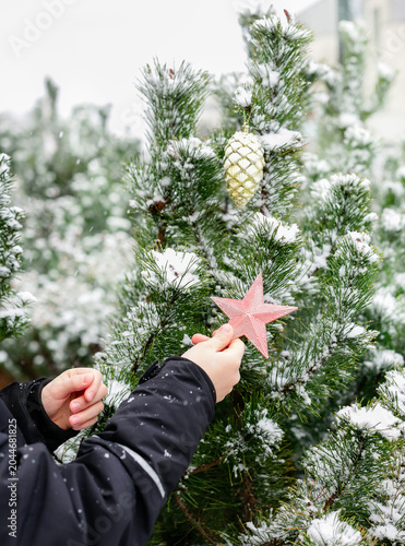Child dressed as Santa with white beard with Christmas tree decorations in snowy winter garden