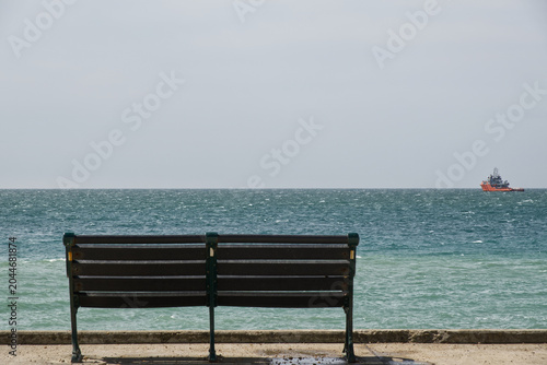 Empty bench on Seafront at Rottingdean near Brighton, East Sussex,  England with boat in distance.