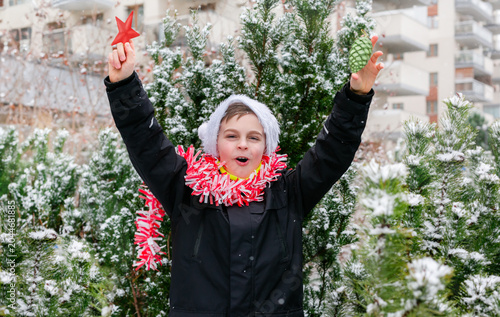 Child dressed as Santa with white beard with Christmas tree decorations in snowy winter garden