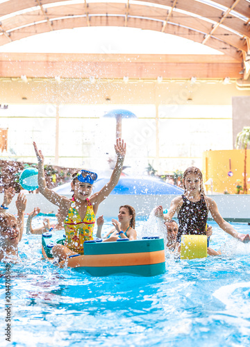 Happy hildren raising hands and playing with pool floats at an indoor water park