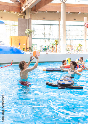 Happy young male friends playing with a beach ball in a large indoor swimming pool at a water park