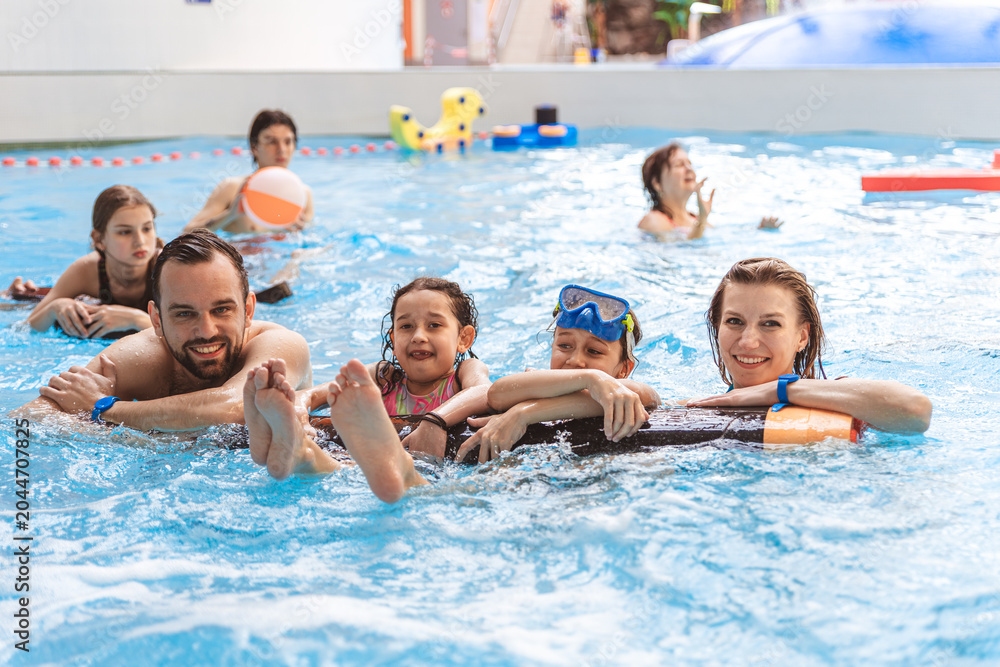 Fototapeta premium Portrait of a happy family smiling and looking at the camera while relaxing with pool floats at an indoor water park