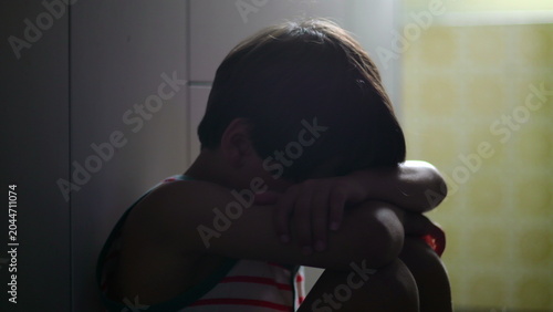 Photos Child sitting curled in kitchen corner hiding face in arms expressing deep sorro
