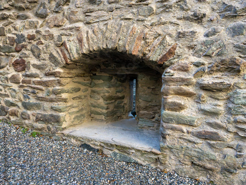 Schilderij op canvas Close-up view of a historic fortress defensive masonry wall, featuring a small stone-arched embrasure with a narrow vertical arrow slit or loophole for defense