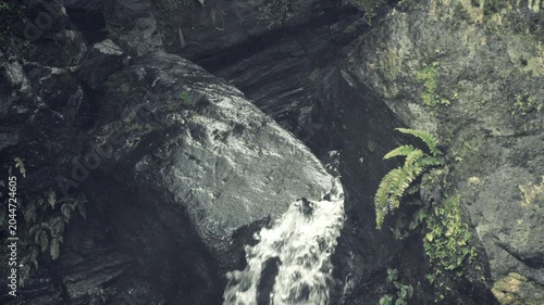 Small Waterfall Rushing Over Dark Rocks in Forest Gorge