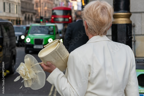 Fotografie London, United Kingdome - May 5th 2023: An elegantly dressed up lady carrying a bouquet waiting at the sidewalk while traffic passes