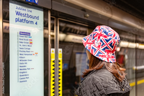 Konstfotografi London, England: A lady wearing Union Jack hat looking at the metro map at one of the underground  stations in the British capital