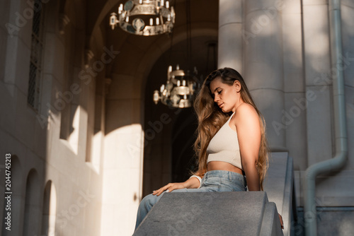 Fotografia Woman, Building, Sunlight - Woman sitting on steps under a chandelier, facing away from the camera, enjoying a sunny day