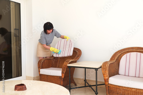 Woman Cleaning Balcony, Dusting Cushions on Chair, Creating a Fresh and Inviting Outdoor Space for Relaxation and Enjoyment.