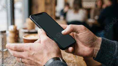 Close-Up of Hands Holding a Smartphone with Blank Screen at a Cafe Table with Coffee