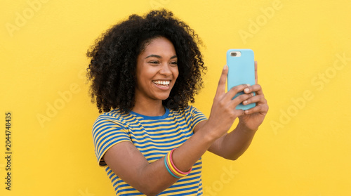 Happy Young Black Woman with Afro Taking a Selfie Against a Vibrant Yellow Background