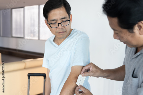 lifestyle shot of a middle aged old southeast asian male grabbing his sore elbow caused by lifting too heavy baggage, with a man come to first-aid with bandage