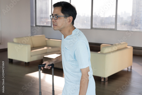 lifestyle shot of a middle aged old southeast asian male grabbing his sore elbow caused by lifting too heavy baggage