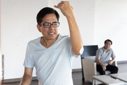 lifestyle shot of a middle aged old southeast asian male grabbing his sore elbow caused by lifting too heavy baggage, feeling the sharp pain