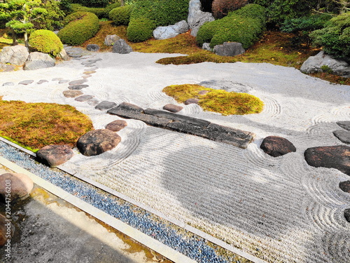 Photos 手入れの行き届いた日本庭園の枯山水風景 白い砂利に描かれた美しい砂紋 苔の島と飛び石が配置され禅の静寂を感じさせる伝統的な庭園の眺め