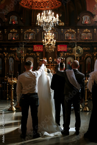 Bild auf Leinwand Wedding in an Orthodox church, witnesses hold crowns over the bride and groom