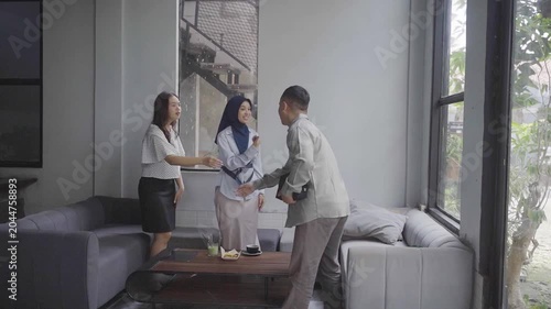 Asian trio seated on sofa negotiating agreement, male consultant standing and addressing two female colleagues including woman