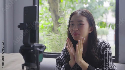 Asian woman storyteller speaking passionately on camera, gesturing with hands, natural window light, phone on tripod, sofa