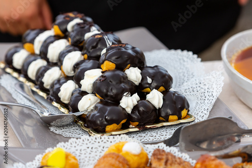 Profiteroles with chocolate glaze and whipped cream topping on buffet