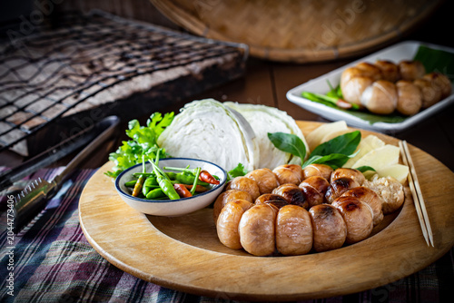 Foto Grilled Thai Isaan sour pork sausage served with fresh cabbage, chilies, and herbs on a wooden plate