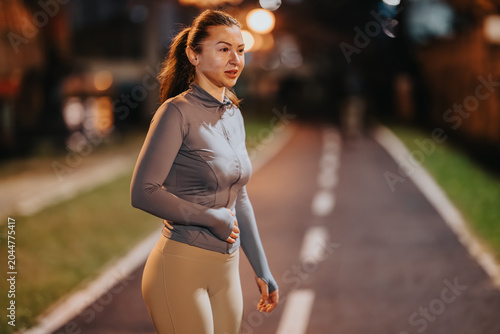 Foto Young woman running along a lit urban path at night wearing workout clothes
