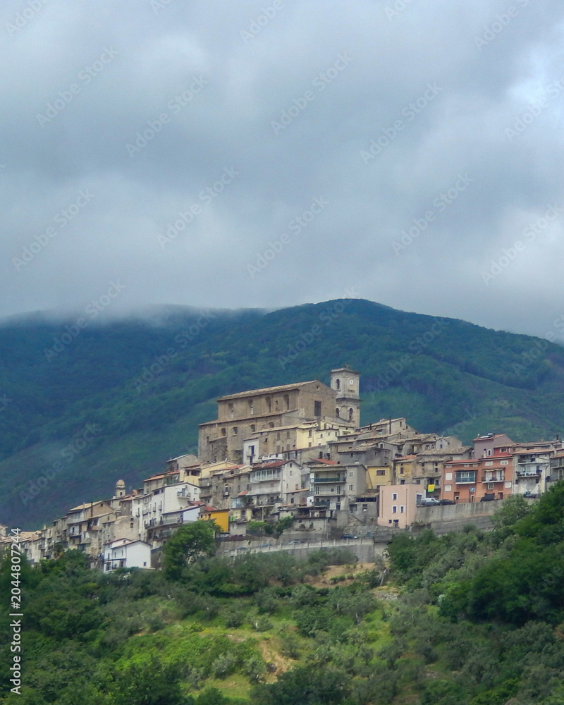 Fototapeta premium Historic village on a hill with buildings and mountains in the background under cloudy sky