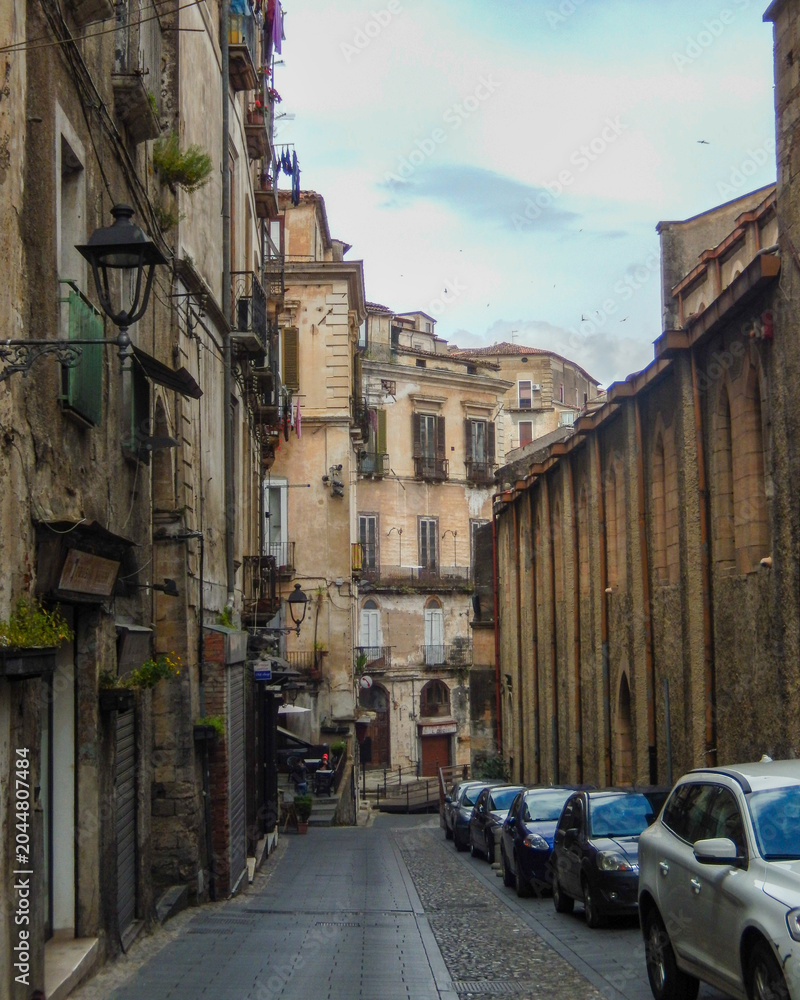 Obraz premium Narrow street with buildings and parked cars in an old city during cloudy weather in the late afternoon