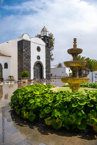 Foto A fountain surrounded by green plants is in front of San Bartolome Church in Lanzarote