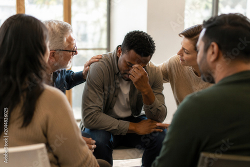 Group gathers around emotional man in therapy session