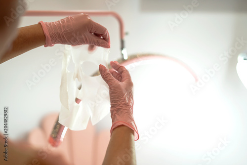 Schilderij op canvas Cosmetologist hands preparing hydrating sheet mask for facial