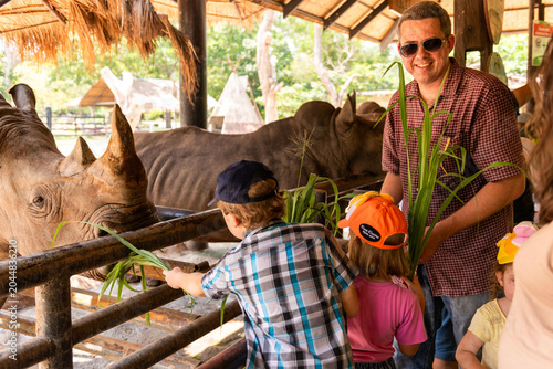 Obraz na plátně Smiling white man and children feeding rhinos at a zoo
