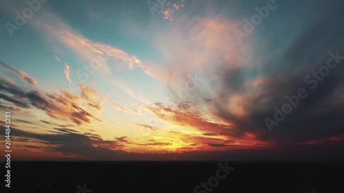 The golden and orange rays of the setting sun burn the edges of the clouds, contrasting with the fading blue sky and the thick, slowly moving gray clouds.